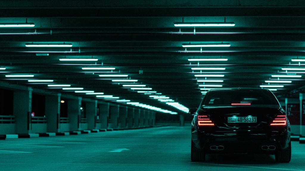 A sleek black car illuminated by neon lights in an empty parking garage, exuding a modern vibe.