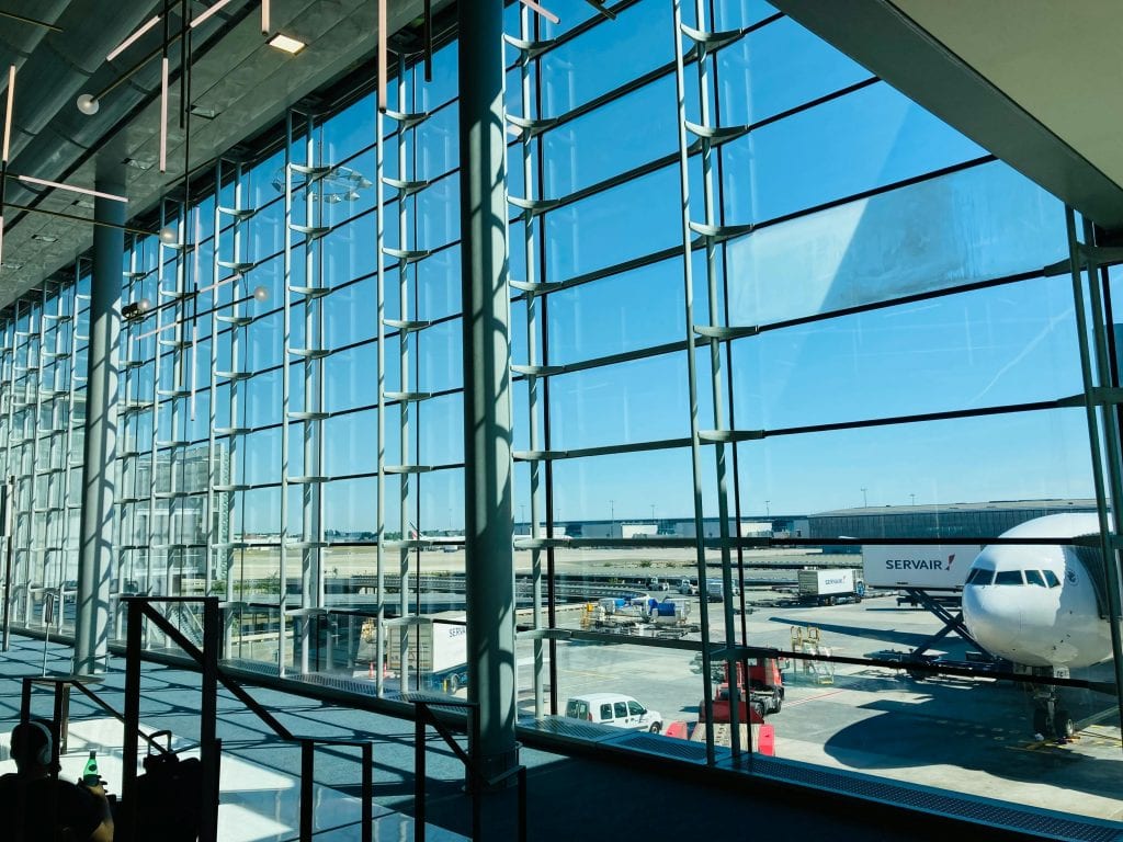 Spacious airport terminal with glass facade overlooking airplane on tarmac.