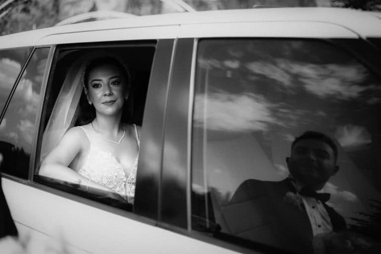 A bride and groom share a reflective moment in a car, captured in black and white.