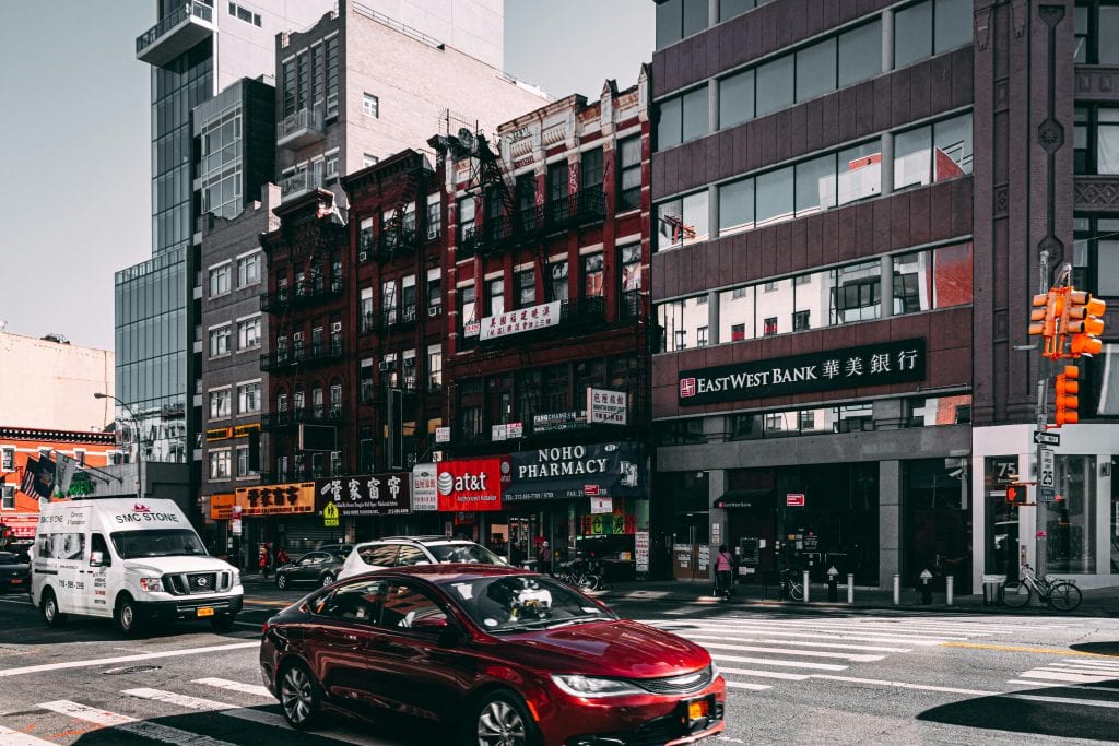 Vibrant street view of Chinatown in NYC with cars and diverse architecture under a bright sky.