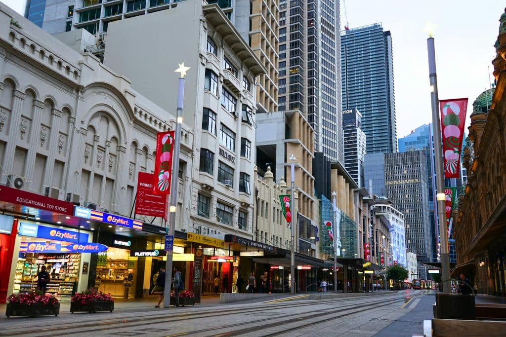 A bustling Sydney street scene featuring shops, historic buildings, and skyscrapers under twilight.