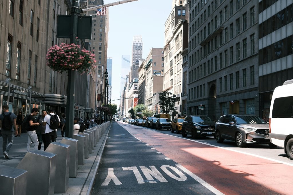 A lively street in New York City with people, cars, and tall buildings under a clear sky.