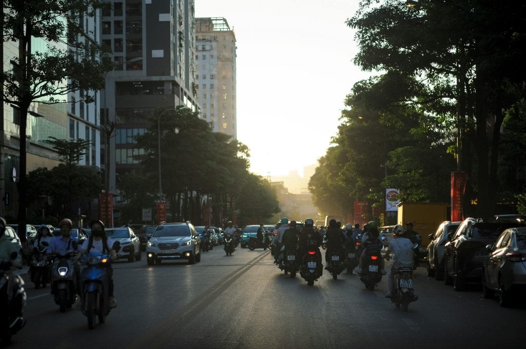 A busy urban street in Hà Nội, Vietnam, filled with cars and motorbikes during sunset.