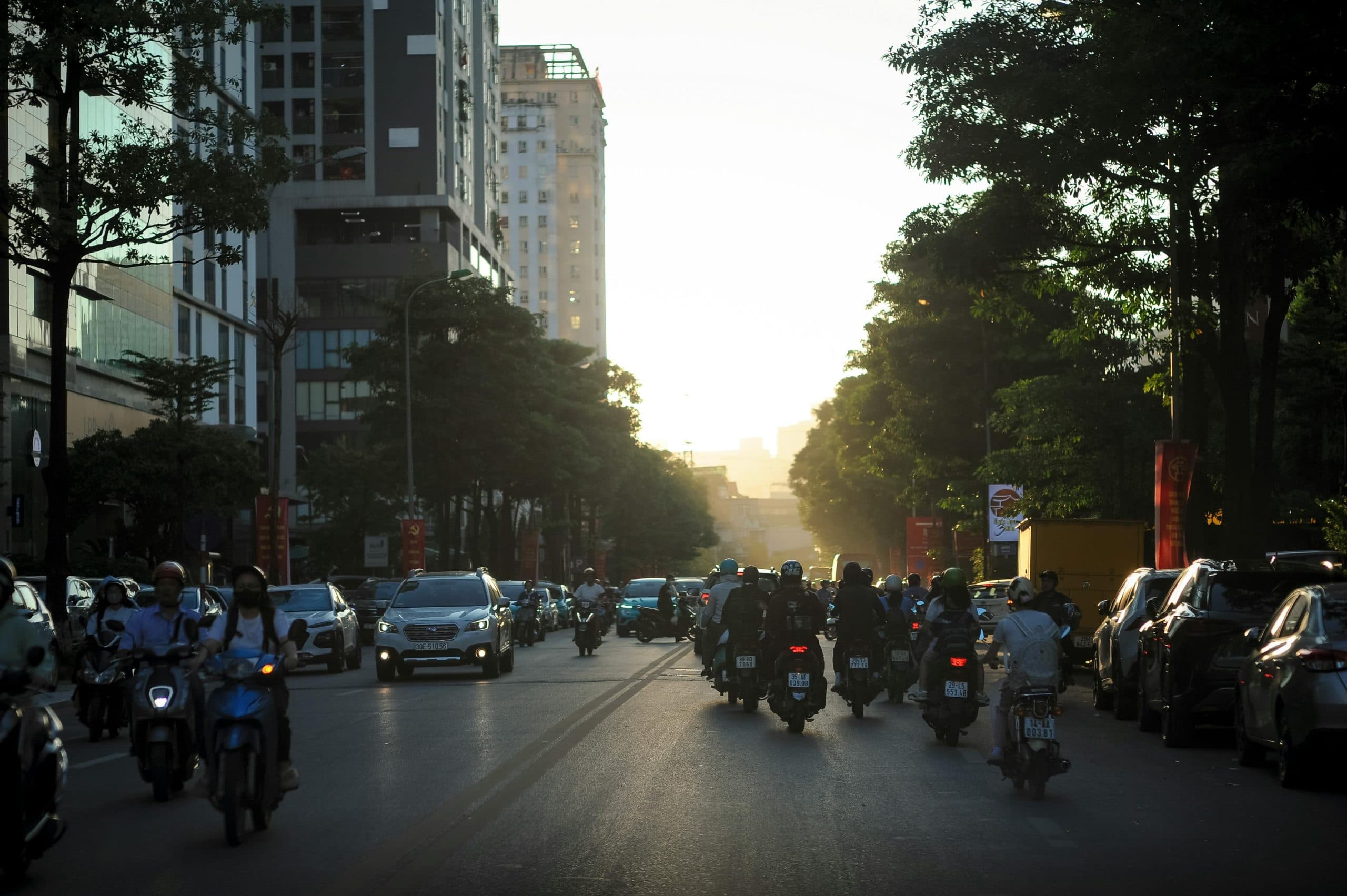 A busy urban street in Hà Nội, Vietnam, filled with cars and motorbikes during sunset.