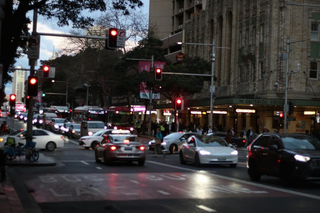 A bustling street in Sydney, Australia, captured at twilight with traffic and illuminated buildings.