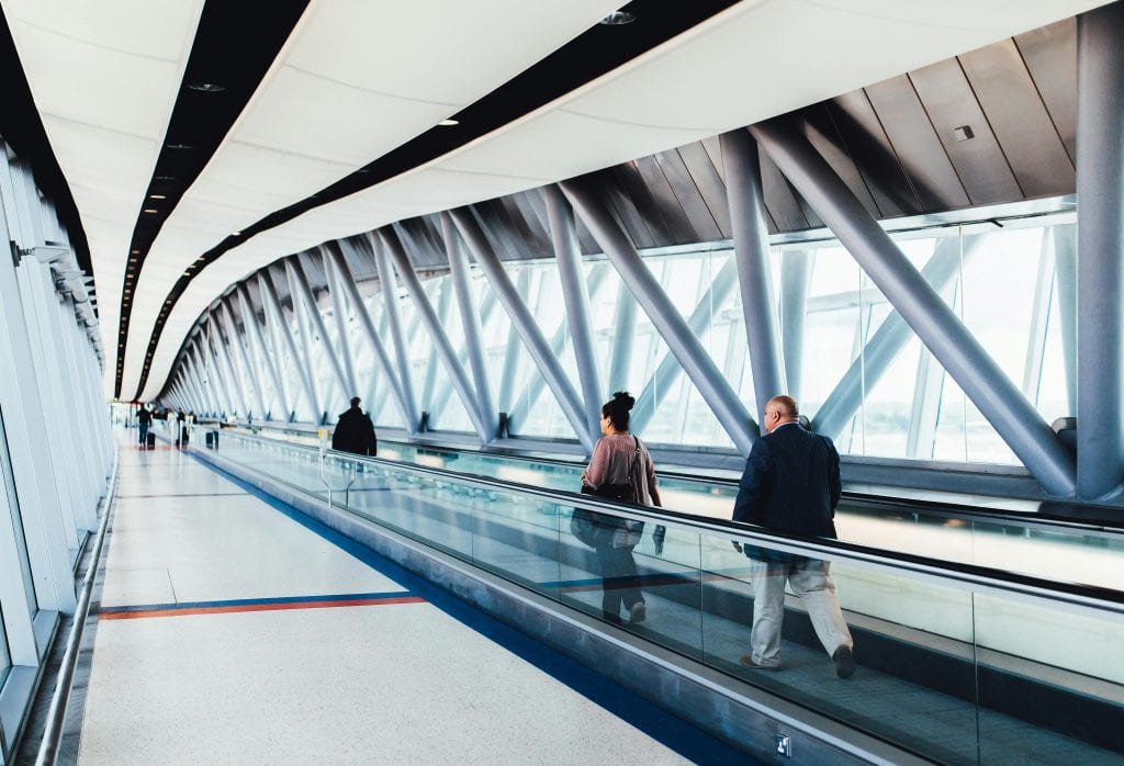 Cheapest Ride to Newark Airport: 6 Honest Options for Families in 2026 3 Travelers walking through a bright modern airport corridor with glass walls.