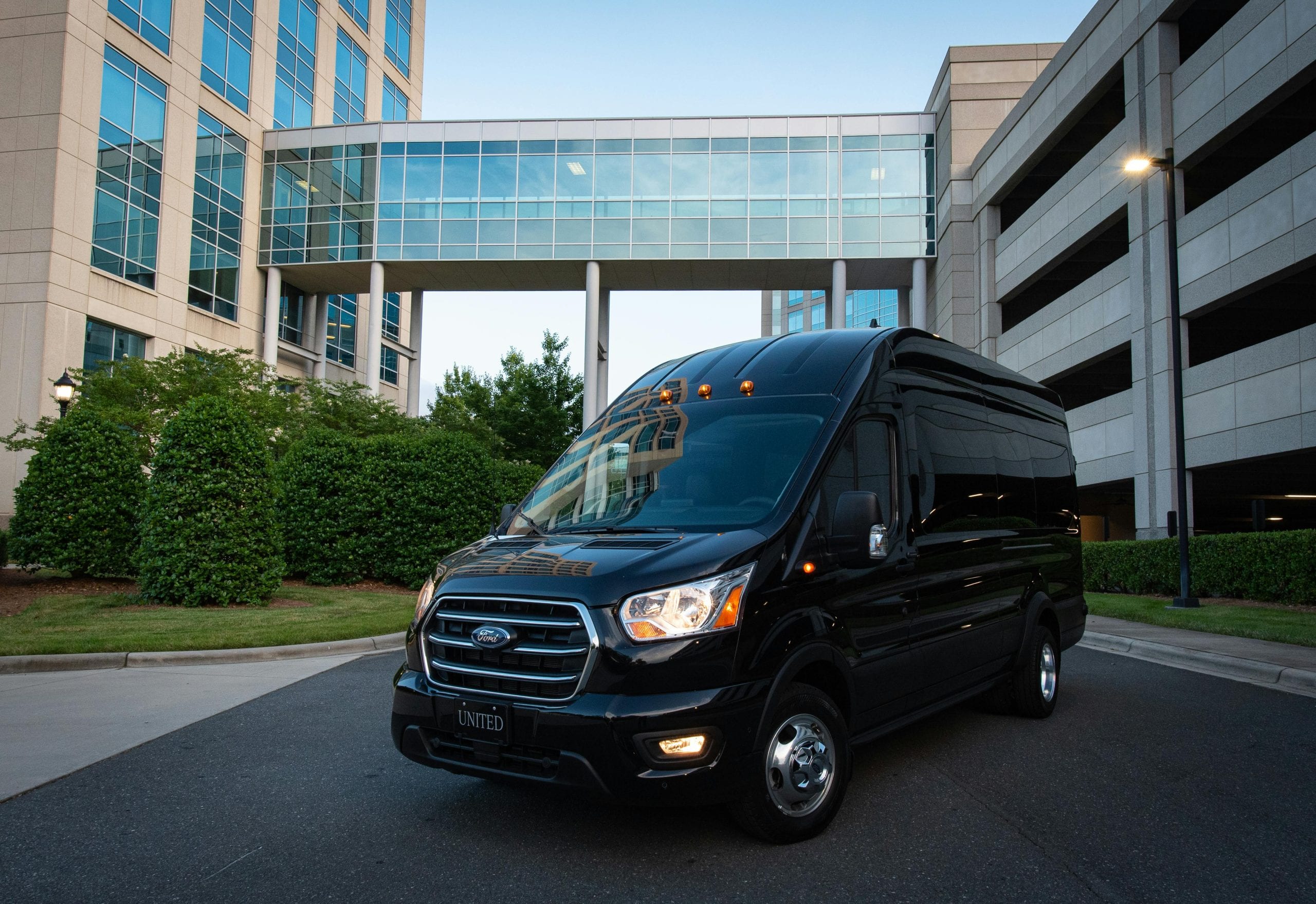 Black van parked in front of a modern building complex with glass walkway and greenery.