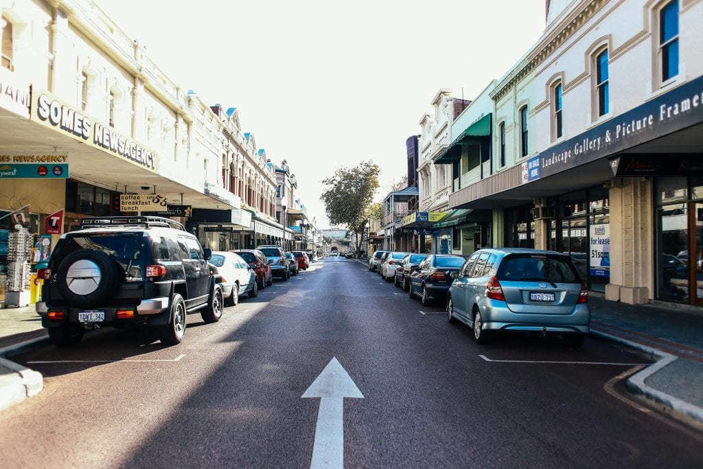 Vibrant city street with parked cars and local shops on a sunny day.