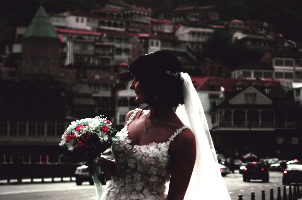 Bride in white gown holding bouquet with cityscape background, exuding elegance and grace.
