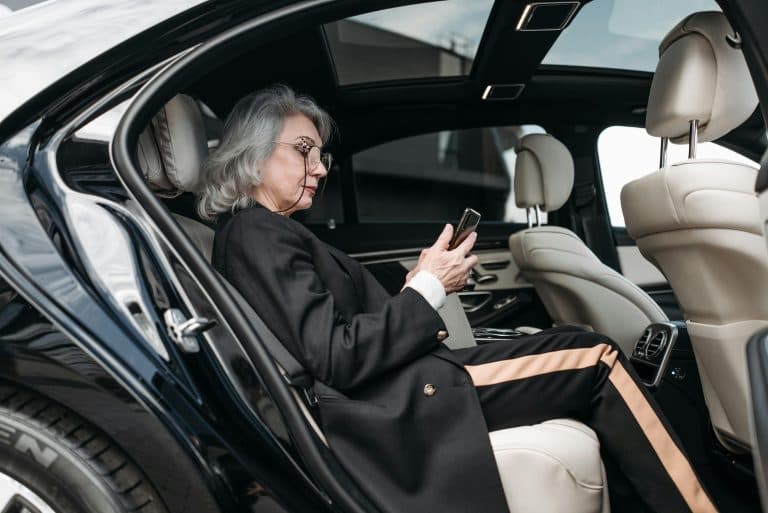 Senior businesswoman sitting in luxury car using a smartphone, showcasing elegance and modern technology.