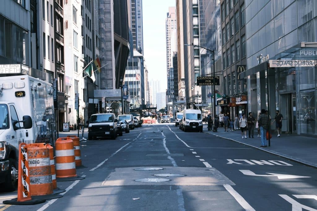 Street view in New York City with vehicles, skyscrapers, and pedestrians on a sunny day.