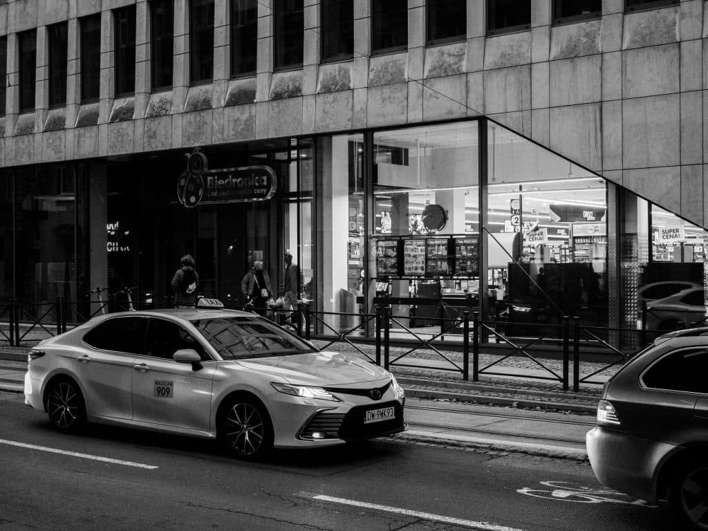 Dynamic urban street scene in black and white featuring a taxi in front of a city store.