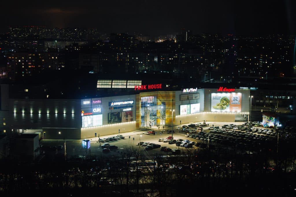 Aerial night view of a shopping mall with bright lights and a busy parking lot.