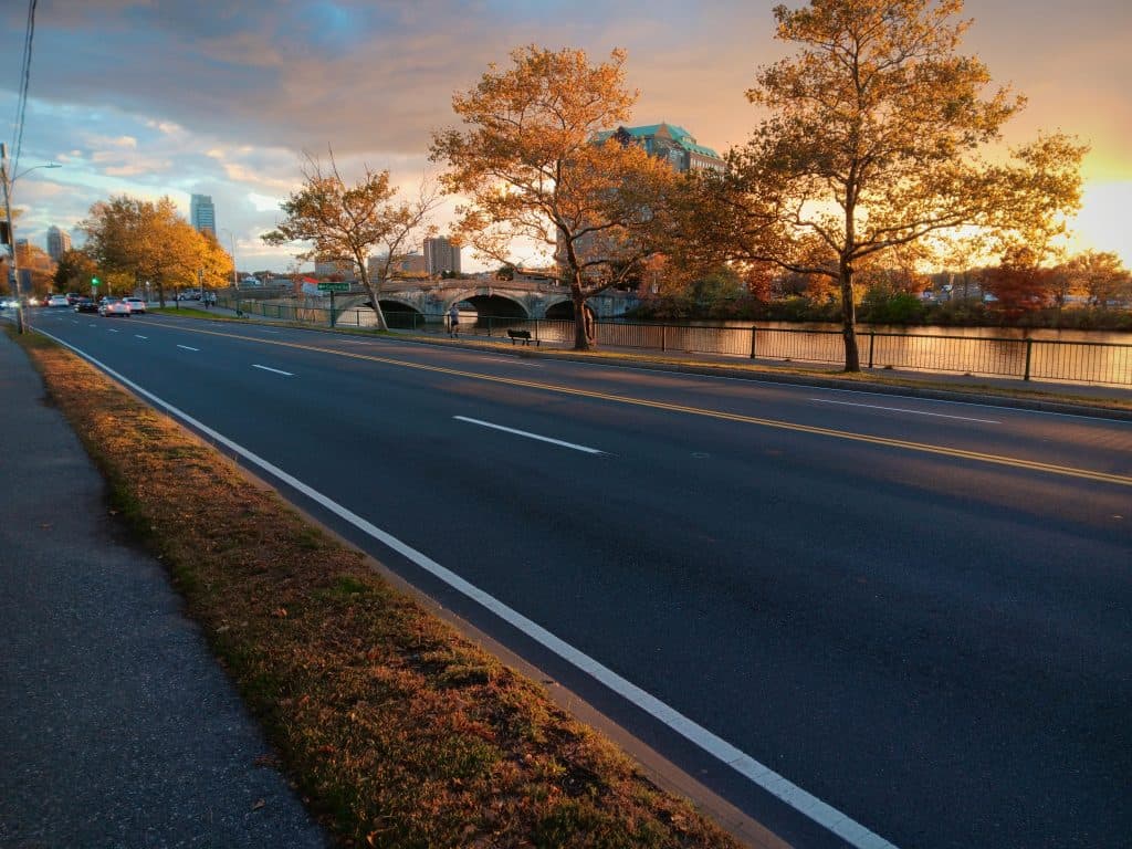 A serene sunset view of an empty road lined with autumn trees beside a river.