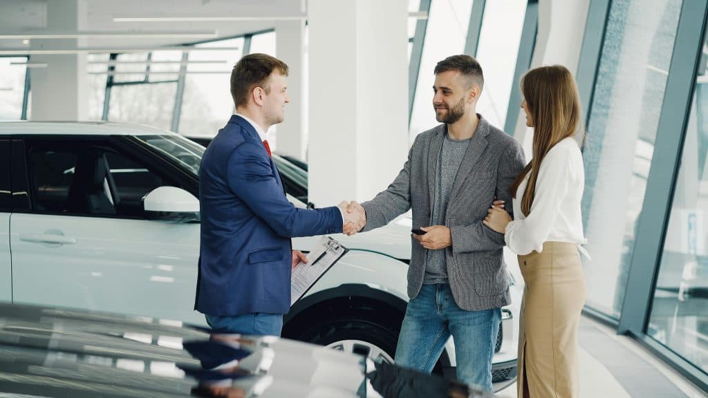 Eco Friendly Limo Deals NYC: 6 Honest Facts for 2026 3 A couple completes a transaction with a salesman at a modern car dealership.