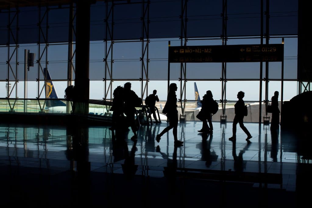 Limo Deals NYC for Airport Transfers in 2026: Fixed-Rate Black Car Service That Actually Delivers When You Need It Most 3 Silhouettes of people walking in an airport terminal, plane tail visible outside.