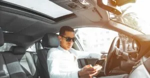 A man wearing sunglasses texts on his phone while driving a car in Morocco.
