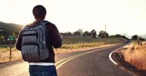 A traveler with a backpack walks on a winding road in the countryside during sunset, symbolizing adventure and freedom.