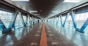 A wide indoor airport passage with tactile paving and steel beams, showcasing modern architecture.