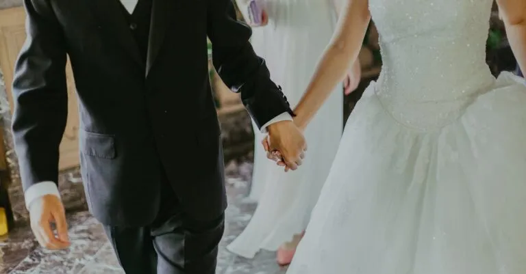 A romantic moment capturing a bride and groom holding hands in elegant wedding attire indoors.