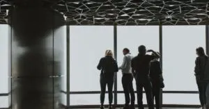 Group of people viewing cityscape through large glass windows in a Dubai skyscraper. Modern architecture and urban exploration.