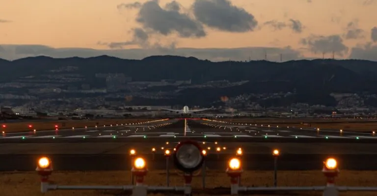 Scenic view of airplane landing on Osaka runway during dusk with city skyline.