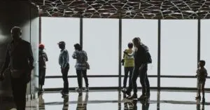 Silhouettes of tourists observing the Dubai skyline from an indoor observation deck.