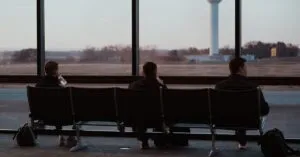 People sitting in airport terminal, watching runway scenes through large windows.