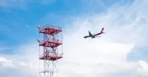Airplane approaches communication tower against a bright blue sky in Sochi, Russia.