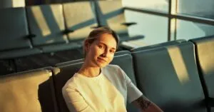 Smiling woman in an airport lounge seat, bathed in warm evening light.