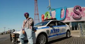 A stylish man in sunglasses poses by a police car at Coney Island, NYC.