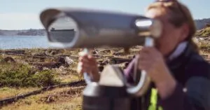 A woman uses a coin-operated binocular to view a distant ship along the Colwood shores.