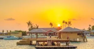Beautiful sunset view at Kanuhura, Maldives with overwater bungalows and serene ocean surroundings.