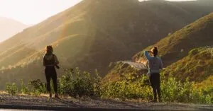 Two hikers enjoying a scenic view of mountain roads at dusk.