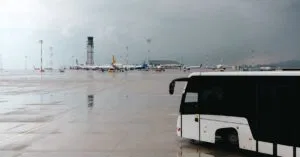 Rainy airport tarmac featuring a passenger bus with airplanes in the background.