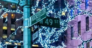 Street sign at Rockefeller Plaza adorned with festive lights in New York City at night.