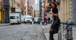 Woman in stylish black outfit poses on a cobblestone street in an urban setting.