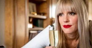 Elegant woman with red lipstick enjoying a glass of champagne indoors.