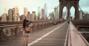 A woman captures the iconic Brooklyn Bridge with the NYC skyline in the background.