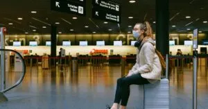 A woman wearing a face mask sits on luggage in an airport terminal amid the pandemic.