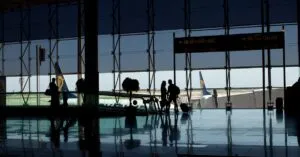 Travelers silhouetted in a modern airport terminal with glass windows and visible airplane tails.