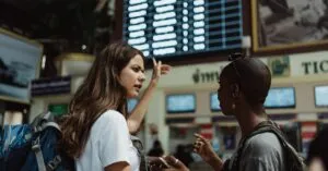 Two travelers with backpacks discuss in front of an airport timetable. Adventure awaits.