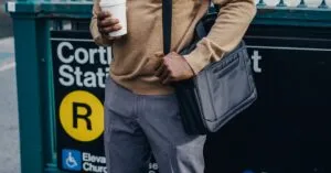 A businessman holding coffee stands by Cortlandt Station subway entrance in a city street.