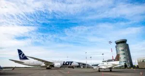 Polish Airlines plane on runway with control tower and jet under a blue sky.