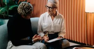 Two professional women engaged in a business discussion indoors with documents.
