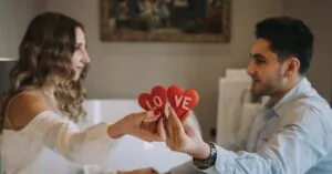 A couple sharing a romantic moment indoors, holding heart-shaped love symbols, enhancing a Valentine's Day feel.