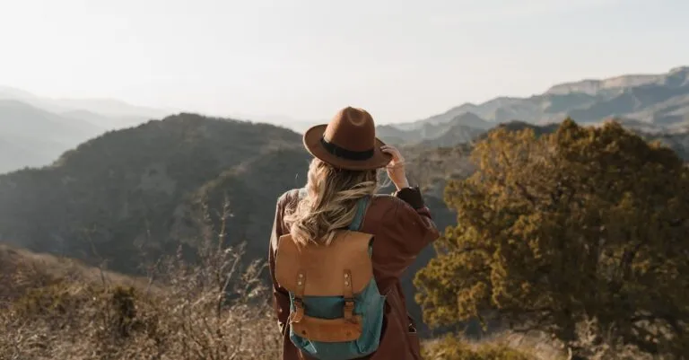 Woman wearing a backpack hiking in mountainous countryside, enjoying the scenic view.
