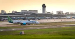 Bamboo Airways airplane on the runway at a busy airport with city skyline in the background.