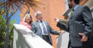 Elderly couple touring a modern home with a real estate agent in sunny Portugal.