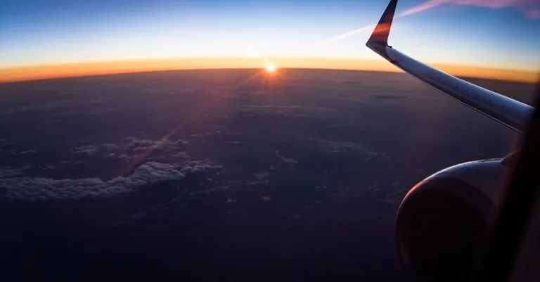Stunning aerial view from an airplane window showing the wing and a sunset over the clouds.